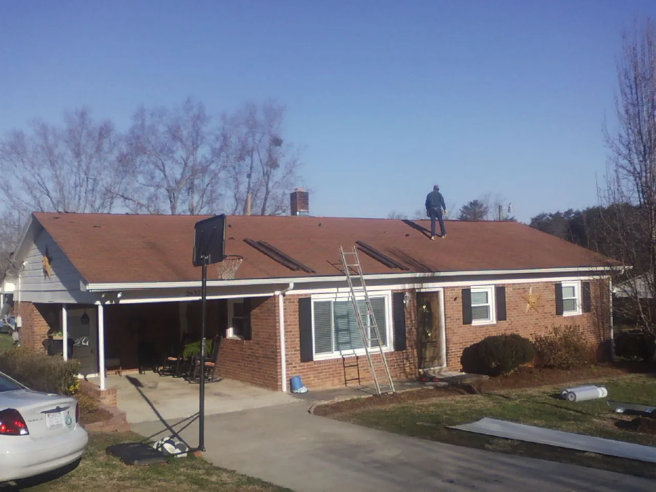Roofer stripping a shingle roof on a brick ranch before metal panels in Marne