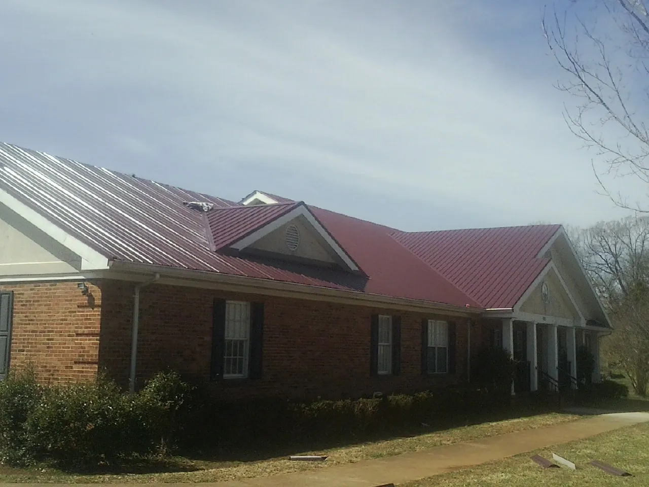 Red metal roof with gabled entries on a long brick building, from a Hail Damage Roof Repair job in Marne