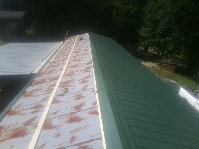Old rusted panels beside newly installed green metal roofing — Wind Damage Roof Repair by Roofing Brothers in Marne