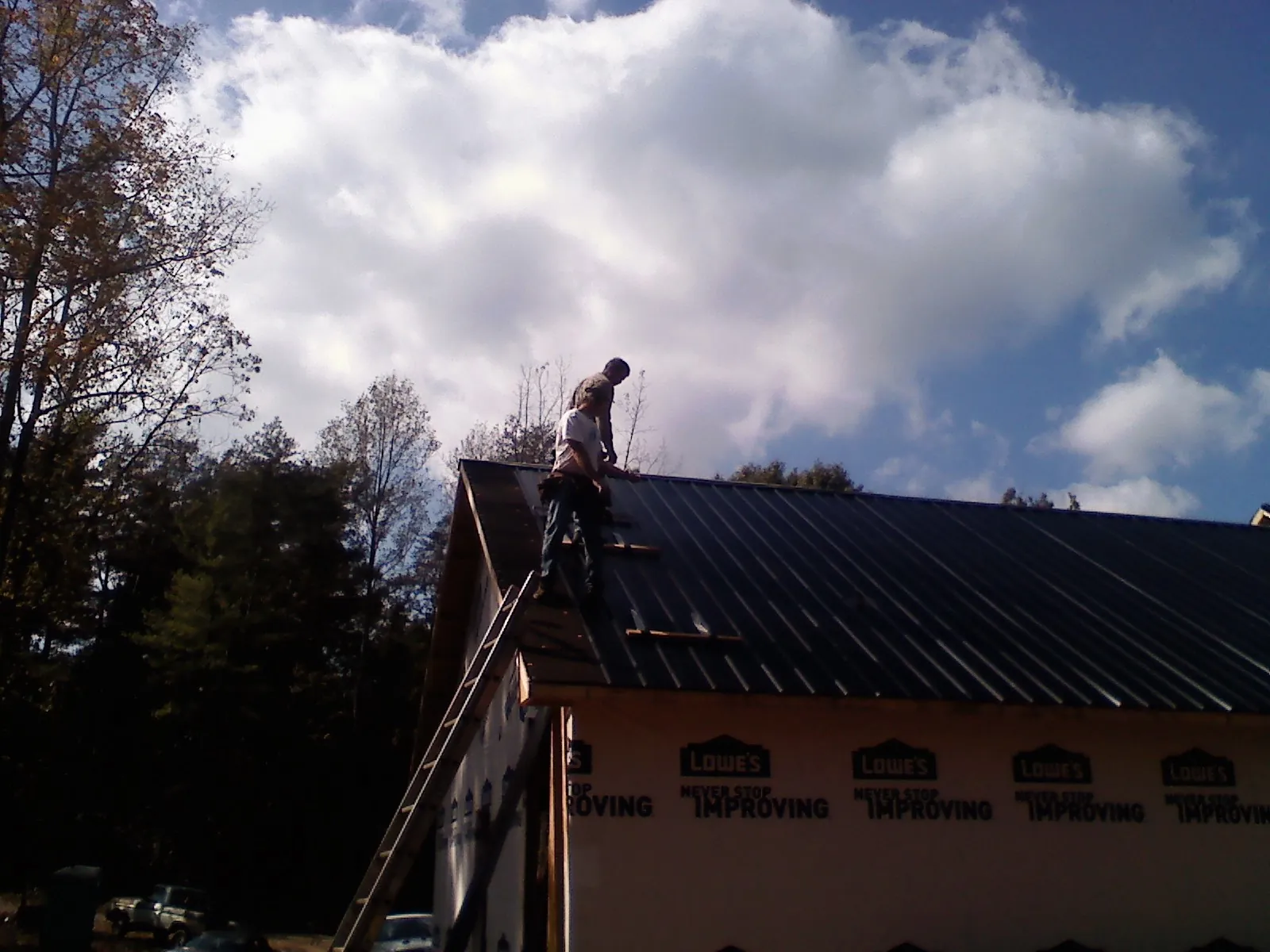 Roofer fastening dark metal panels high against a cloudy sky, from a Roof Inspection job in Marne
