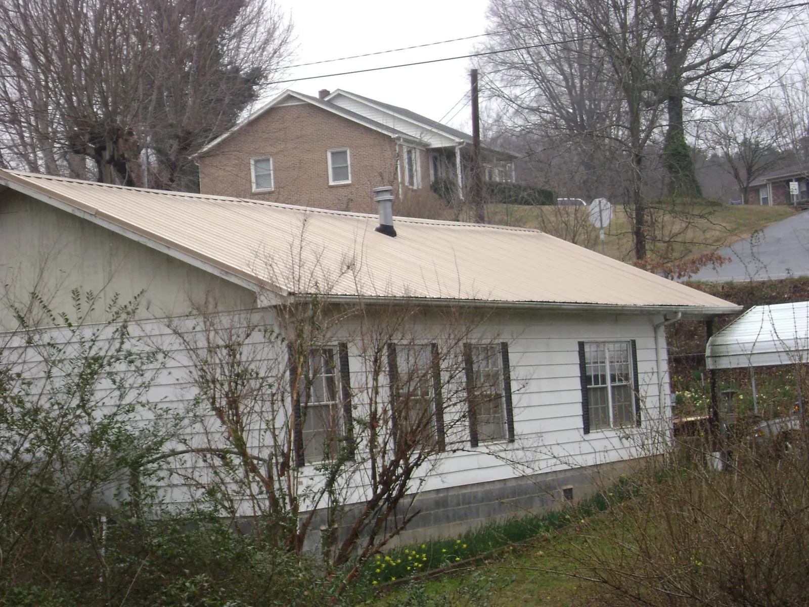 Tan metal roof on a white sided house set into a hillside — Commercial Roofing by Roofing Brothers in Marne